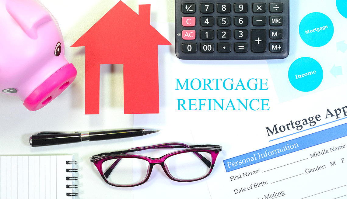 display of items used when considering refinancing the mortgage including eyeglasses, calculator, mortgage application, home and a piggy bank. 