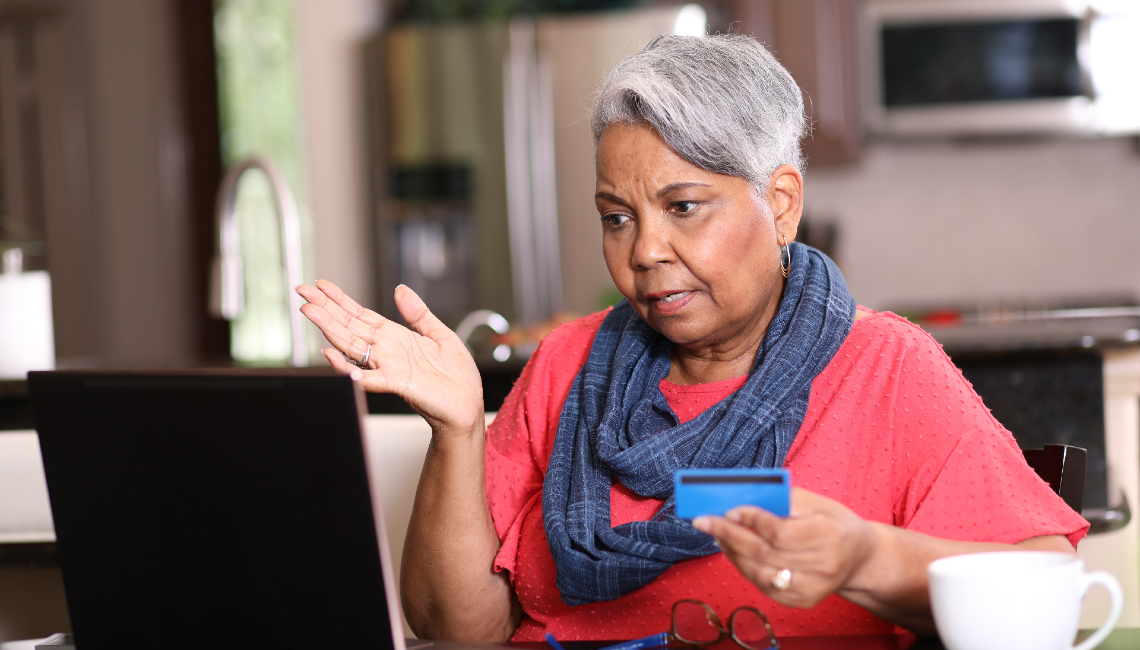 Mujer sostiene una tarjeta de crédito mientras habla desde su computadora
