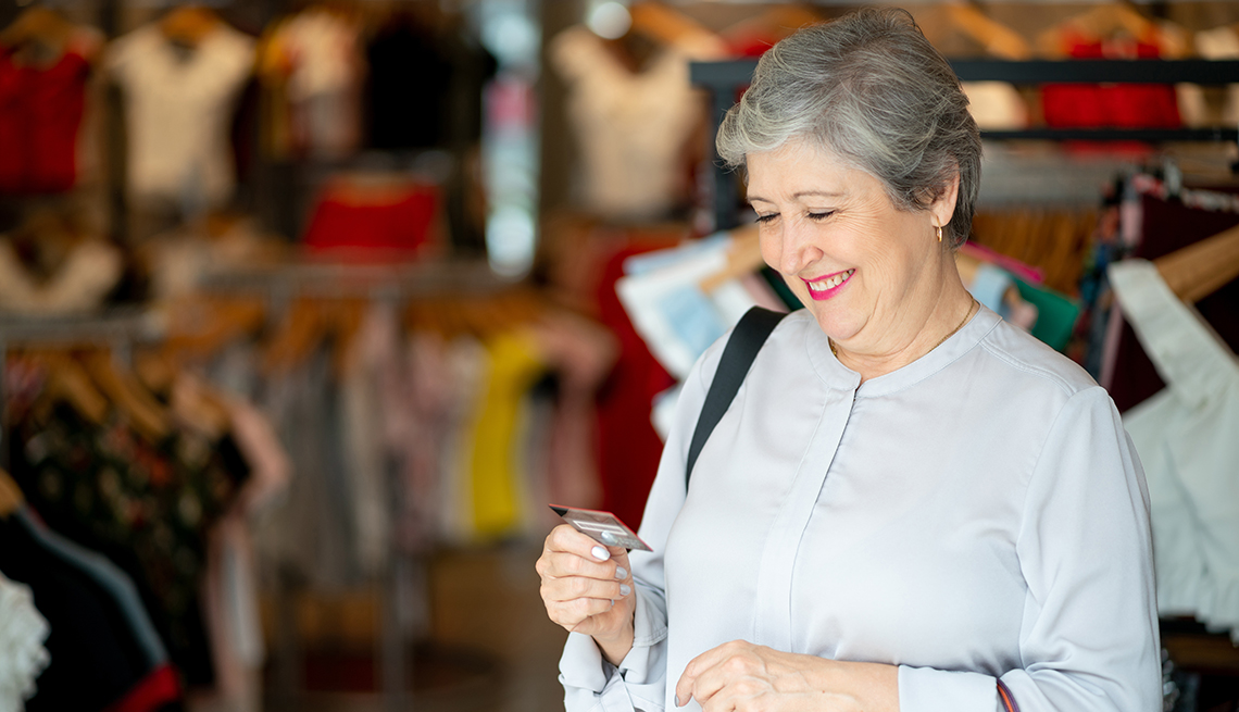 Mujer sonríe mientras sostiene en la mano su tarjeta de crédito en una tienda de ropa