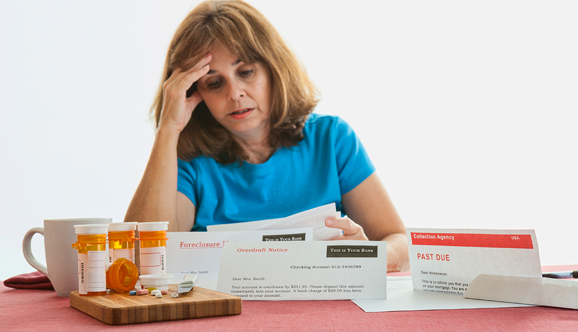 Mujer con cara de preocupación revisa facturas médicas al lado de unos medicamentos.