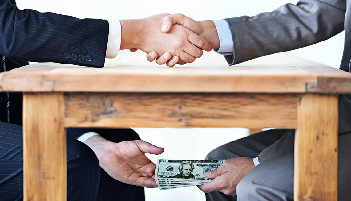 Men in suits shaking hands passing money under table