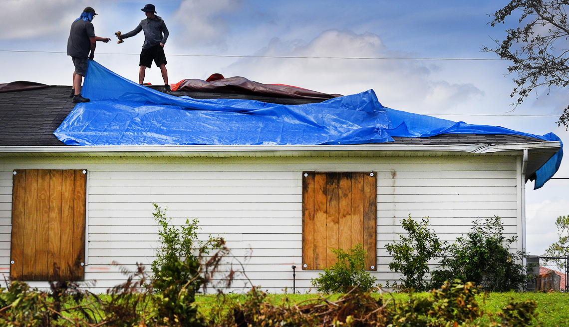 Dos personas reparando el techo de una casa después del paso del huracán