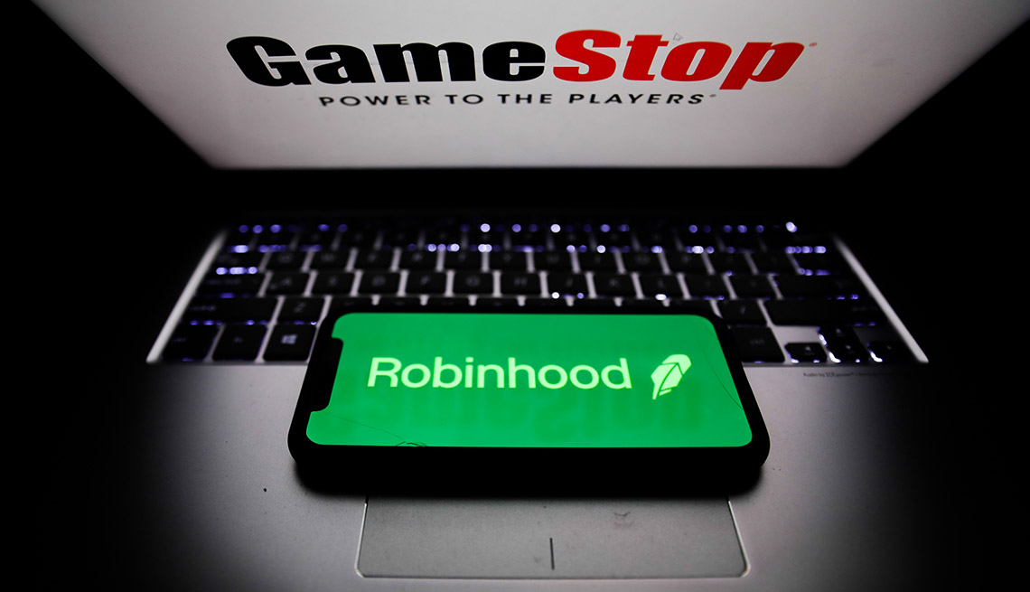 Robinhood stock trading app logo displayed on a phone screen and GameStop logo displayed on a laptop screen