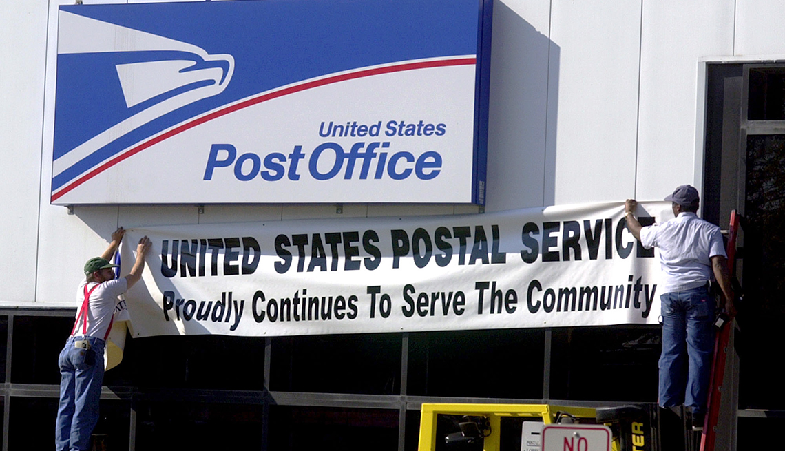 Dos hombres colocando un letrero debajo de la pared exterior de una oficina del correo postal en Hamilton, Nueva Jersey