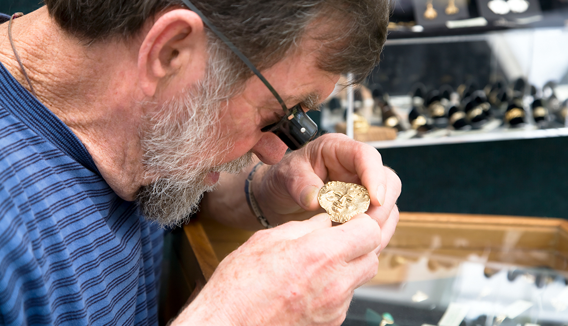A man uses a magnifying jeweler's loupe to closely examine a piece of gold jewelry
