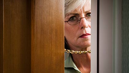 Mujer mirando por la puerta de su casa - Alerta de estafas