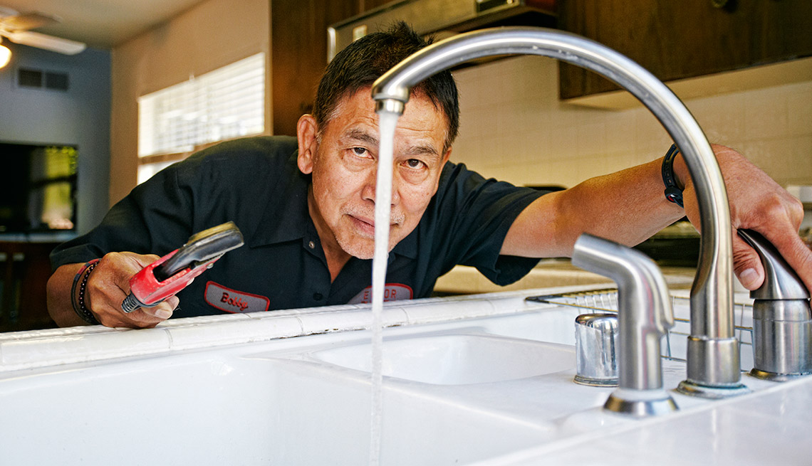 Hombre revisando la plomería de una cocina - Estafas en reparaciones domésticas