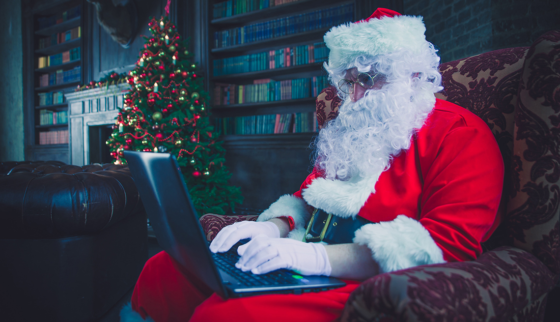 Retrato de Papá Noel Santa en una sala con una computadora portátil en sus piernas.