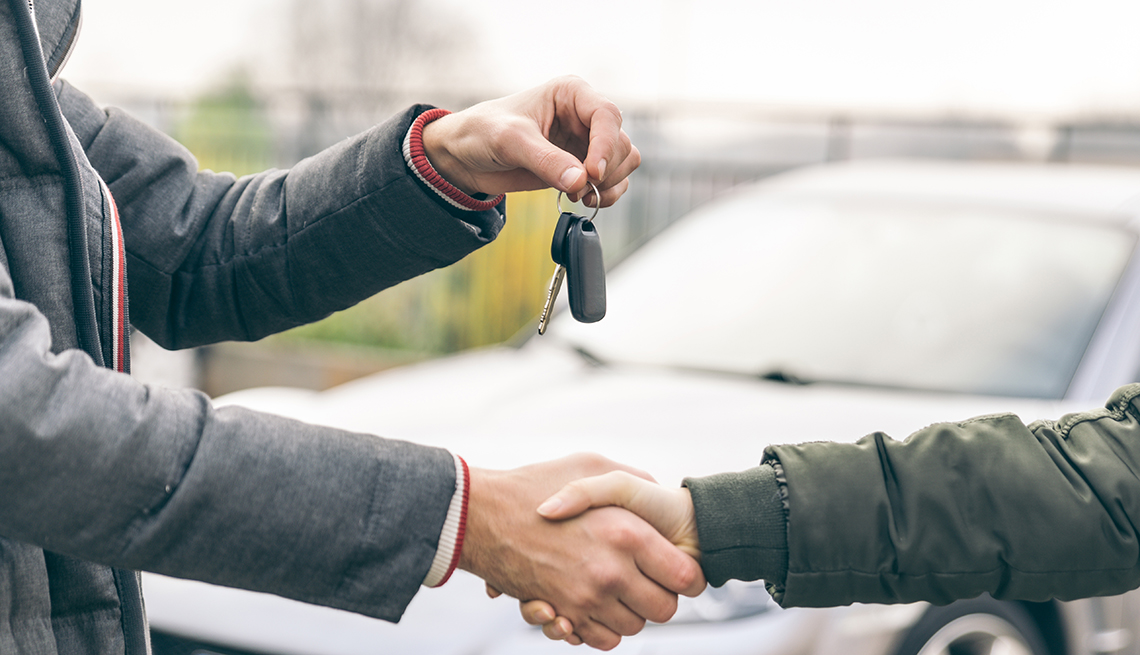 Two people shaking hands as one person hands over car keys, with a car pictured in the background