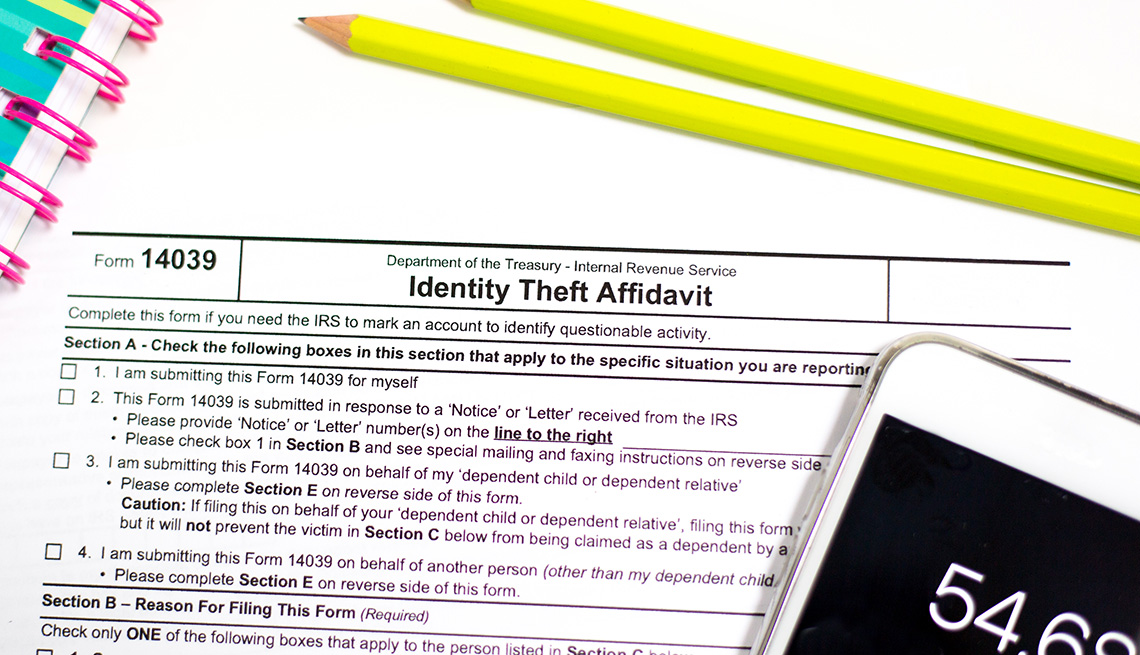 IRS Identity Theft Affidavit, pencils, and a smart phone calculator on a white background.