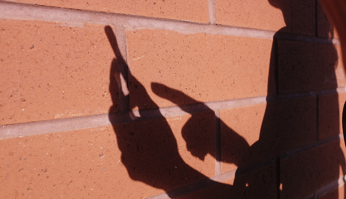 Sombra de una mujer usando un teléfono inteligente sobre un muro de ladrillo