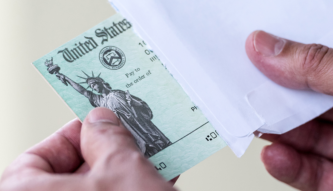 Manos de una persona sacando de un sobre un cheque del Departamento del Tesoro de Estados Unidos.