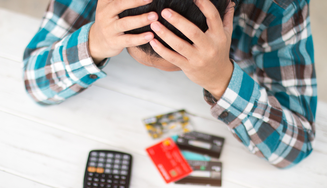 Hombre se sostiene la cabeza con las manos mientras observa una calculadora y sus tarjetas de crédito