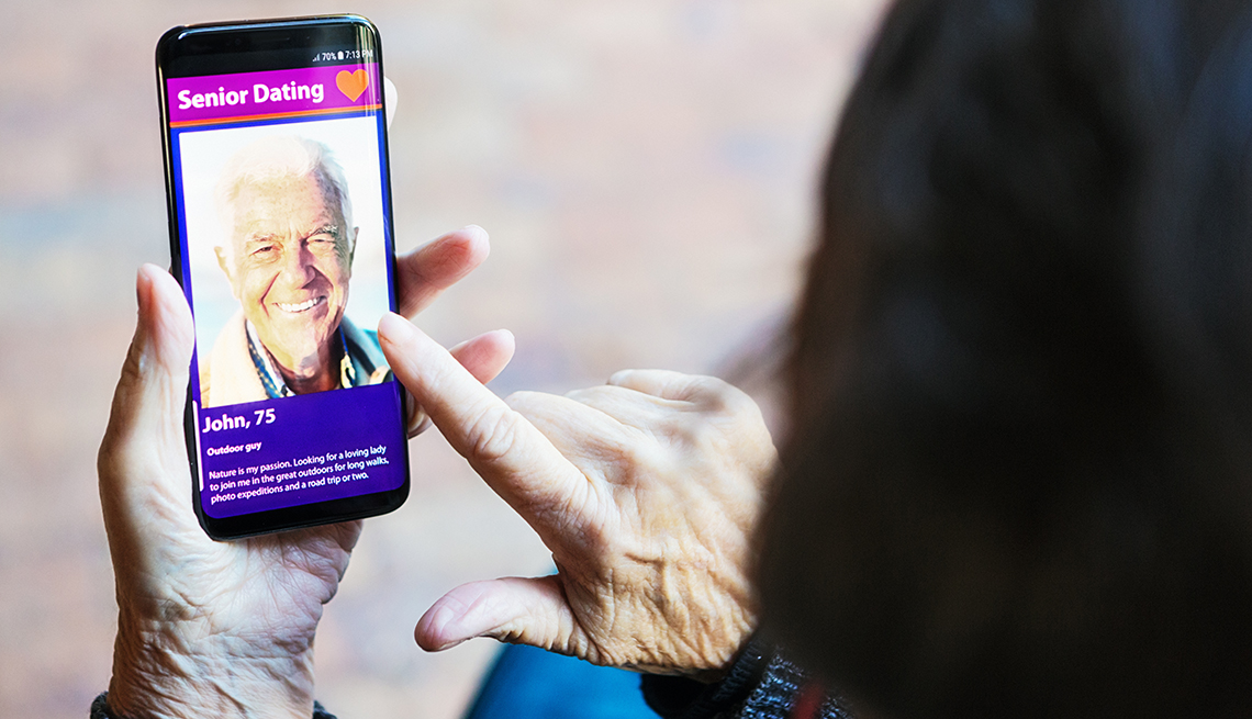 A woman's hand nears a mobile phone screen showing a handsome senior man on a seniors' dating app.