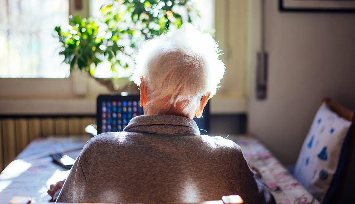 Mujer mayor sentada en un comedor donde ve su computadora para una reunión en línea con su familia