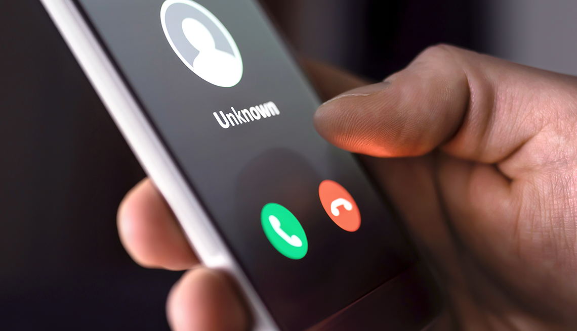 Mano sostiene un teléfono móvil y en la pantalla la llamada de un perfil desconocido con la opción de contestar o colgar