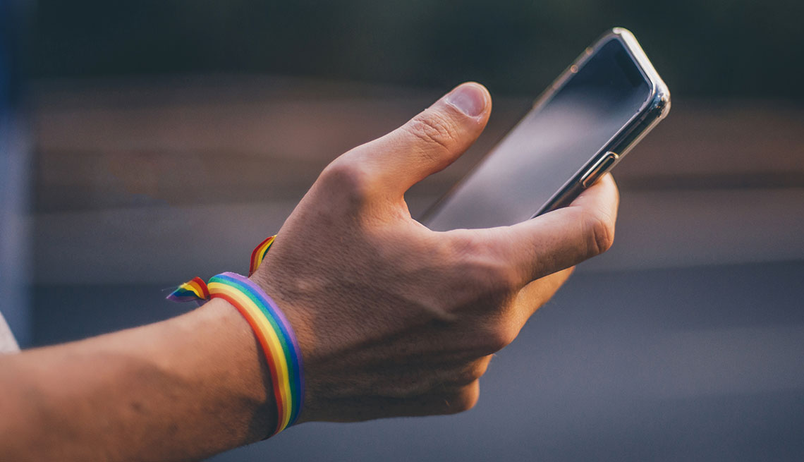 Mano sostiene un teléfono móvil con un bracelte con los colores del arco iris