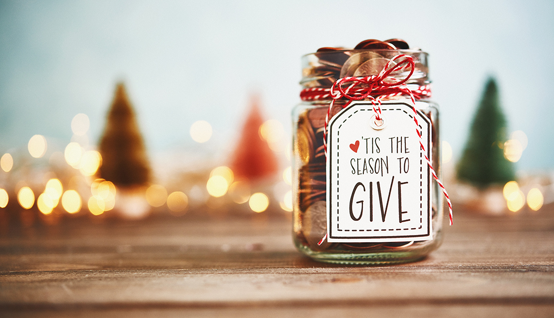 A donation jar with holiday decorations in the background. The jar says 'Tis The Season to Give