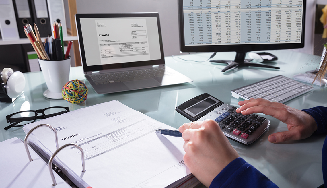 Persona haciendo cuentas en su oficina con facturas, computadora, calculadora, libreta y lapiceros.