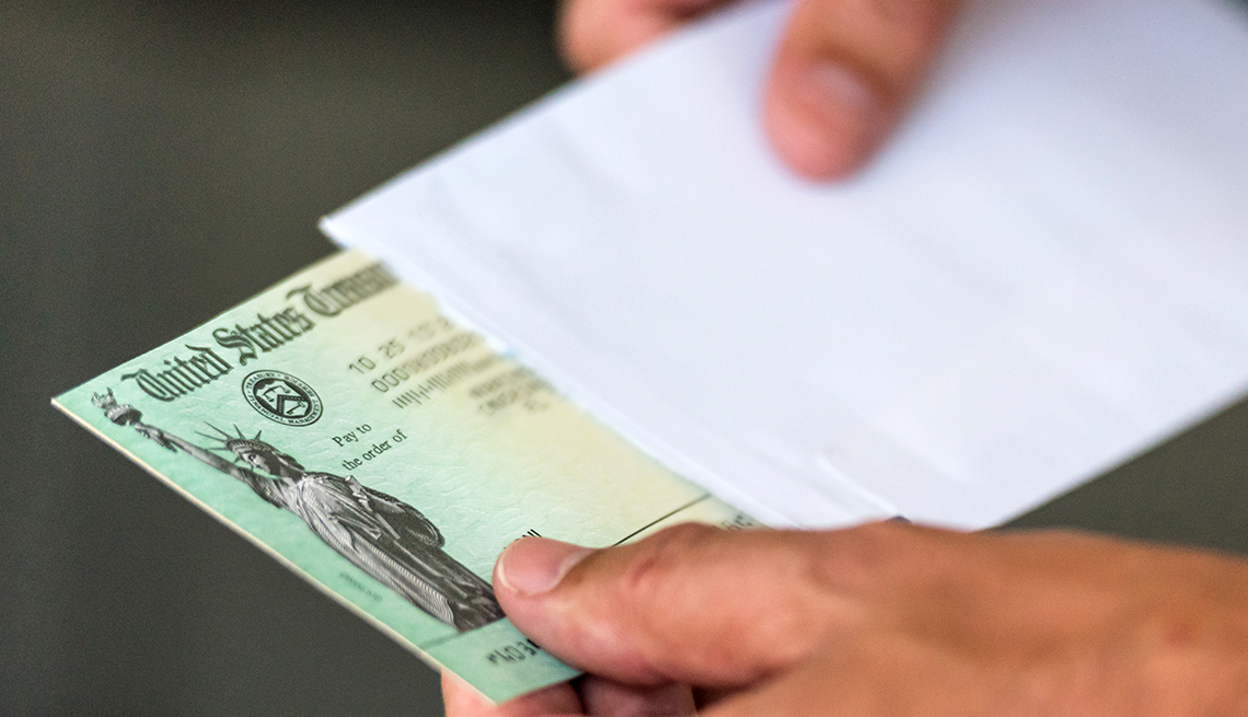 Manos de una persona sacando un cheque del Departamento del Tesoro de los Estados Unidos de un sobre.