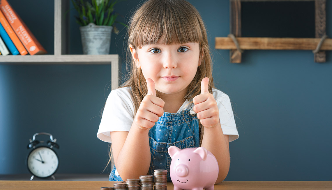 girl giving the thumbs up to saving money as she poses with her piggy bank and piles of coins