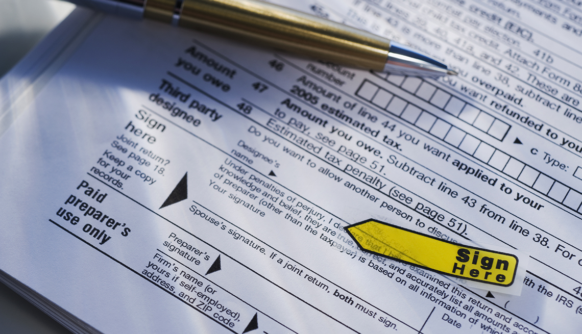 a yellow sticky note label on a 1040 tax form reminds taxpayer to "sign here"