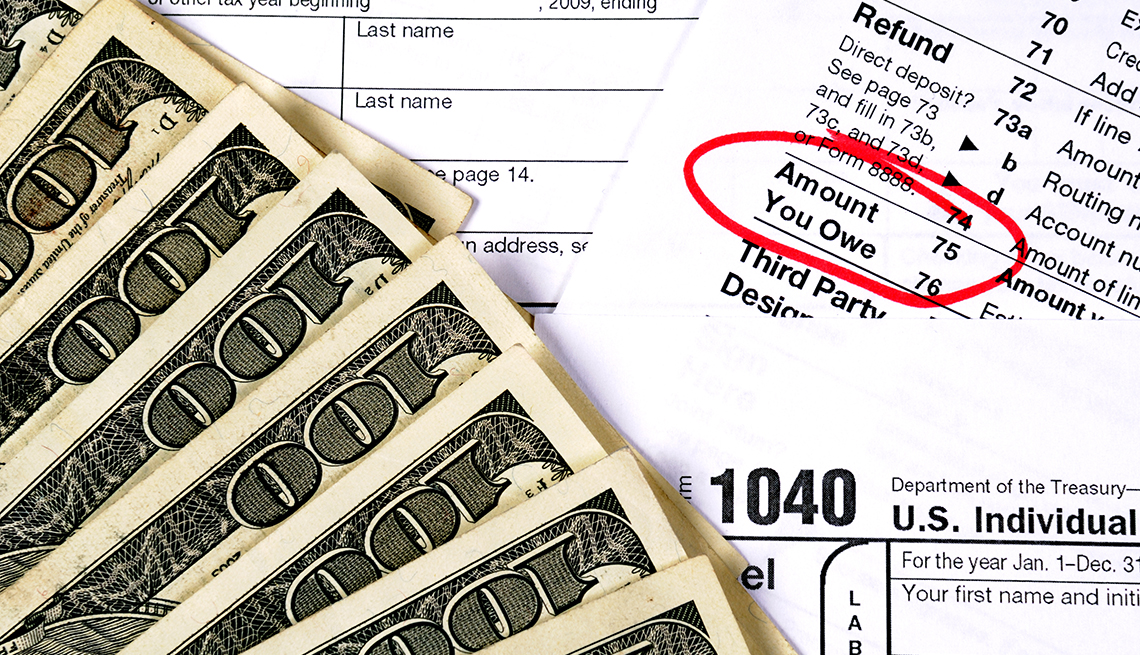 close up of an IRS 1040 tax return form with "Amount You Owe" box circled in red next to a fanned out display of hundred dollar bills 