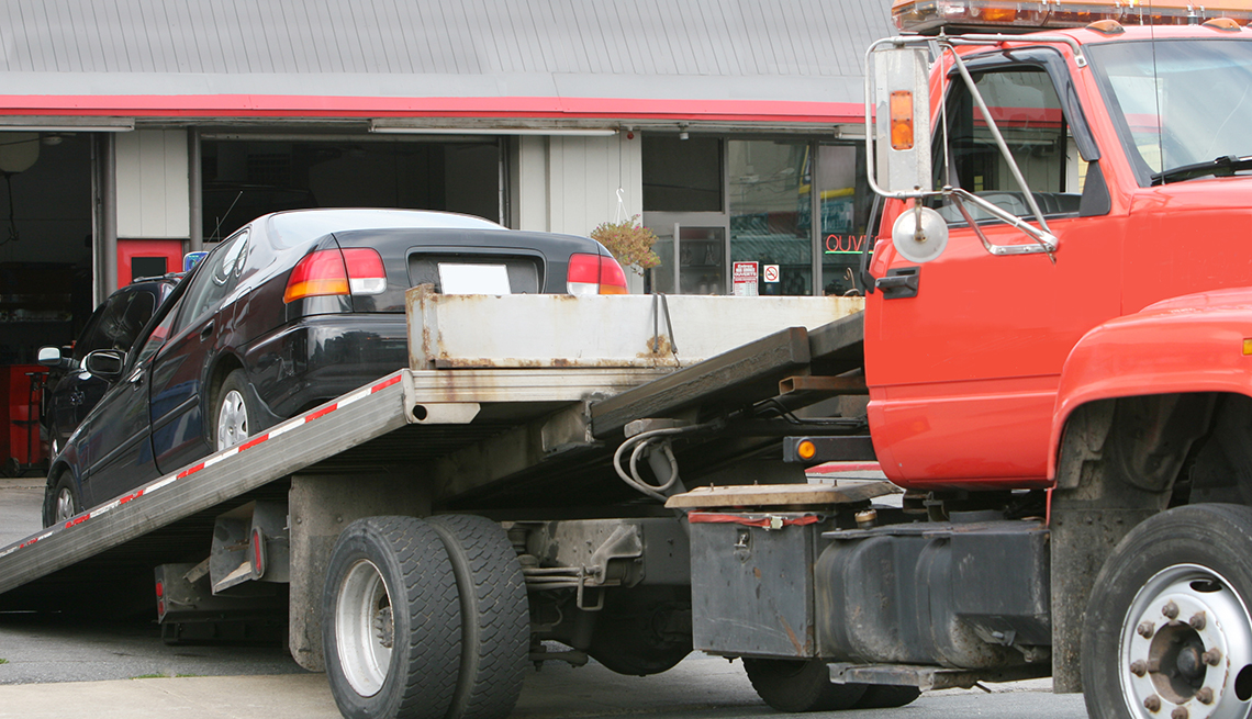 Flatbed tow truck unloading a car to an auto garage shop