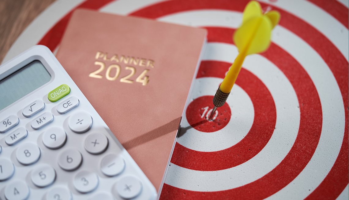 Un dardo ha dado en el blanco en un tablero de dardos, junto a un libro de agenda de planificación para 2024 y una calculadora