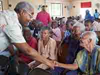 Barry Rand shakes hand with a seated woman at the St. Vincent de Paul nursing home in Leogane where children put on a show for the elderly, Barry Rand visits Haiti