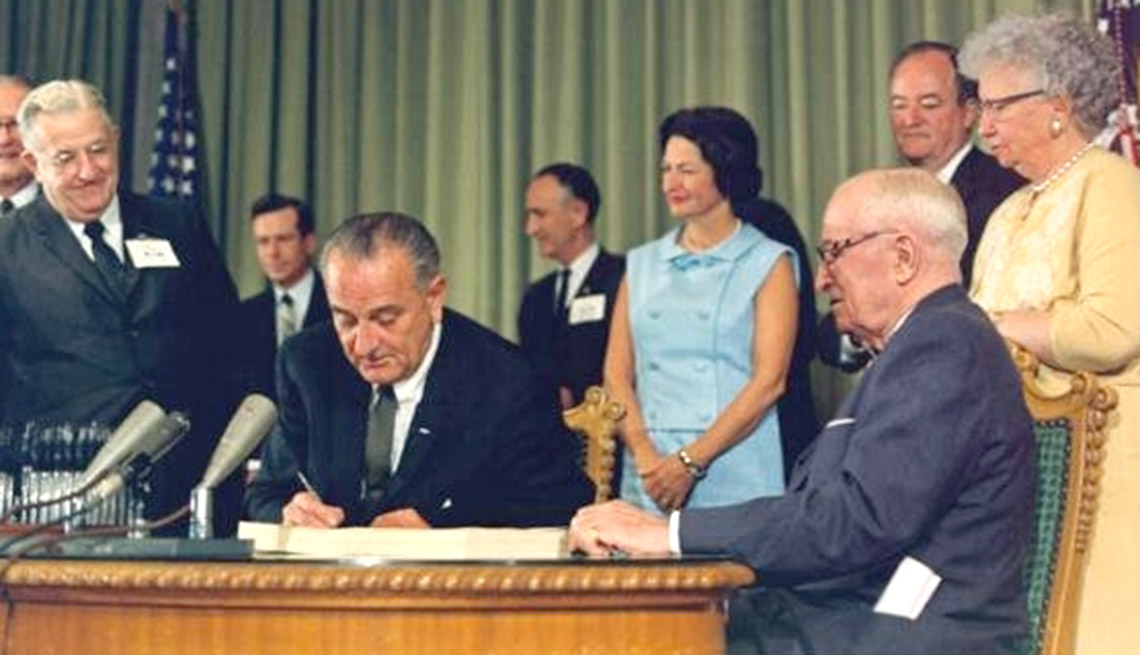 President Johnson signing the Medicare program into law, July 30, 1965. Shown with the President (on the right in the photo) are (left to right) Mrs. Johnson; former President Harry Truman; Vice-President Hubert Humphrey; and Mrs. Truman. 