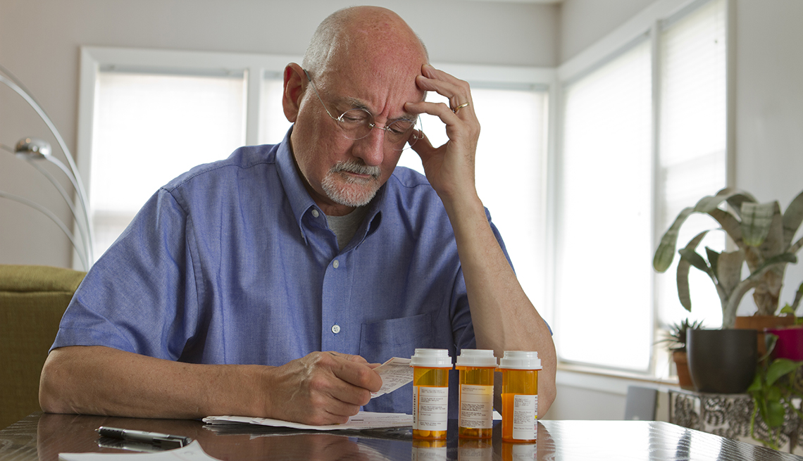 Hombre sentado en una mesa, con tres recipientes de medicinas, mira un papel.