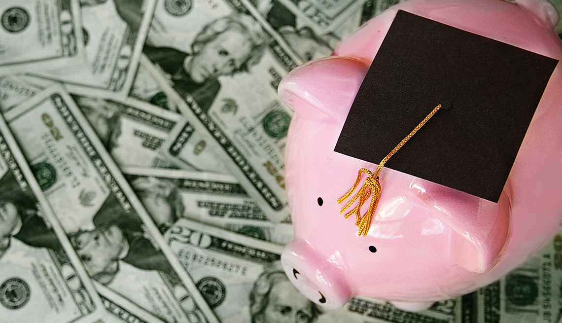 Piggy bank sitting on money with a graduation cap on top of it