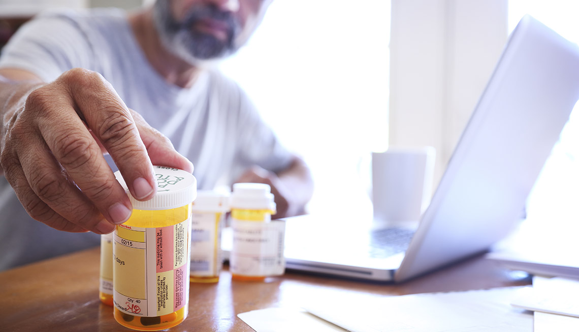 Un hombre adulto mayor alcanza uno de sus recipientes con medicamentos recetados