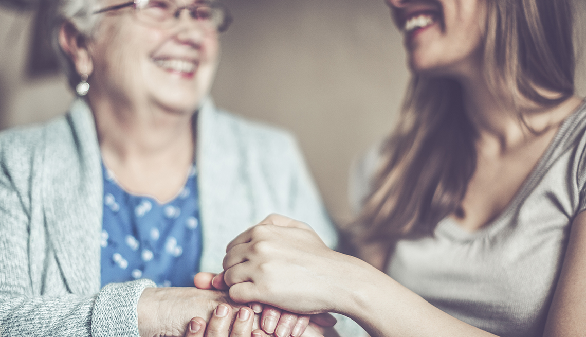 Mujer sostiene las manos de su madre mientras sonríen