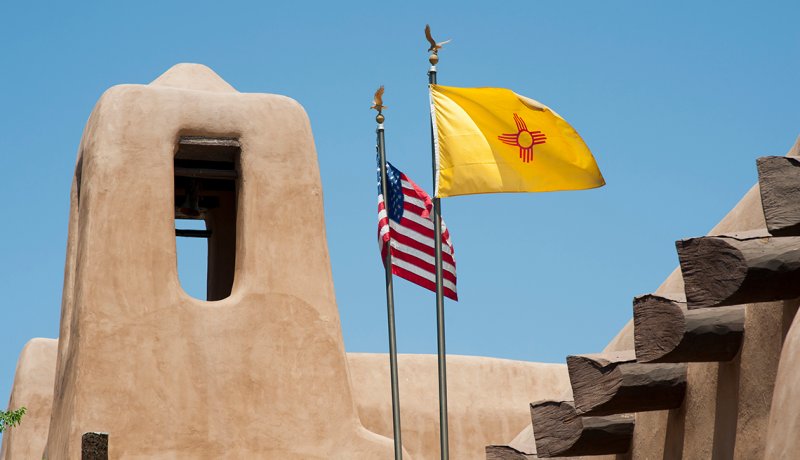 The flags of New Mexico and the United States fly over a building