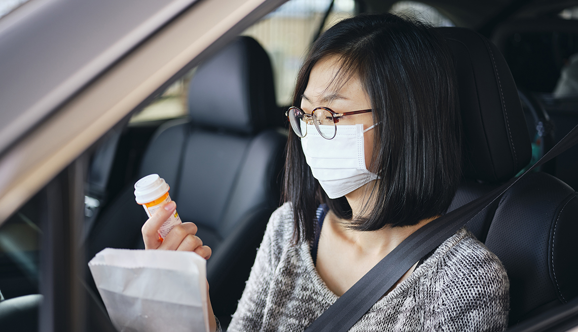 Una mujer con una máscara dentro de su auto mira un frasco de pastillas