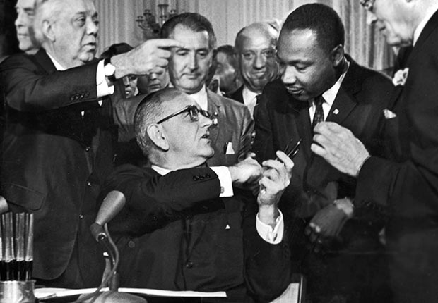 U.S. President Lyndon B. Johnson shakes the hand of Dr. Martin Luther King Jr. at the signing of the Civil Rights Act while officials look on, Washington D.C., Golden Jubilee of the 1964 Civil Rights Act