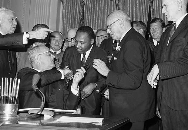 Martin Luther King, Jr. standing next to President Johnson as he signs the Civil Rights Act