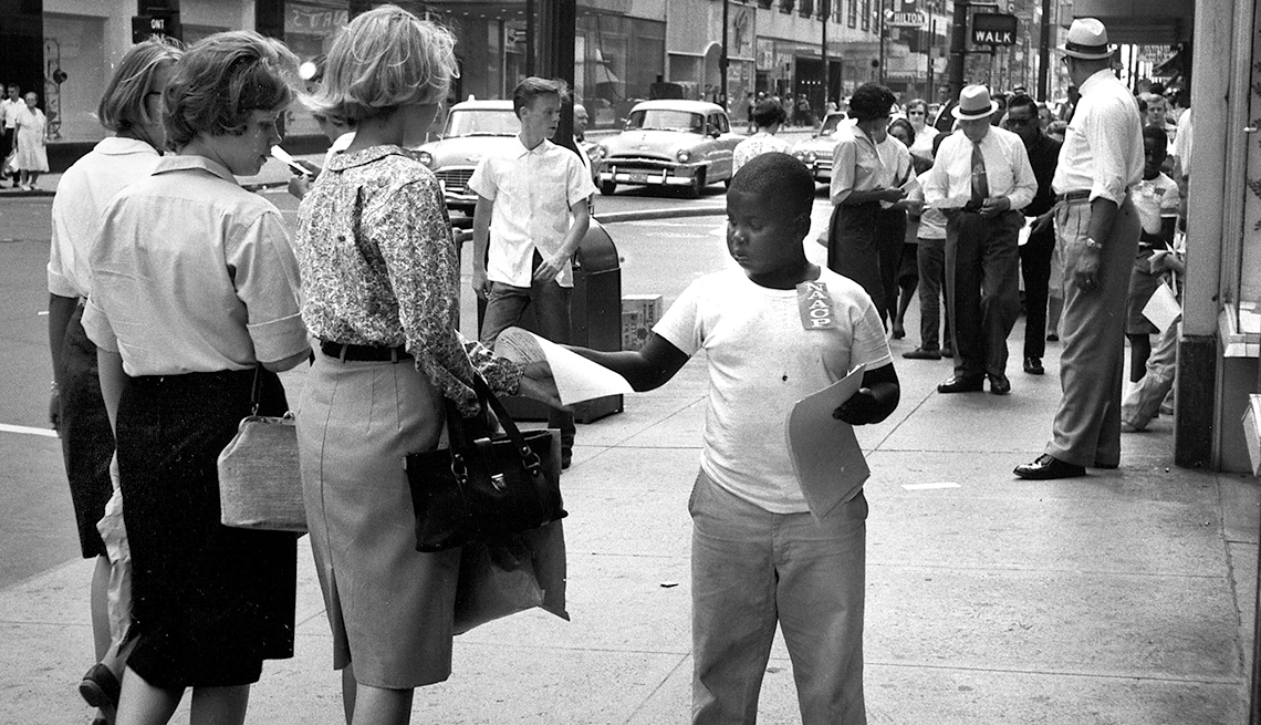 Niño negro entrega un boletín informativo a unos transeúntes - 1963