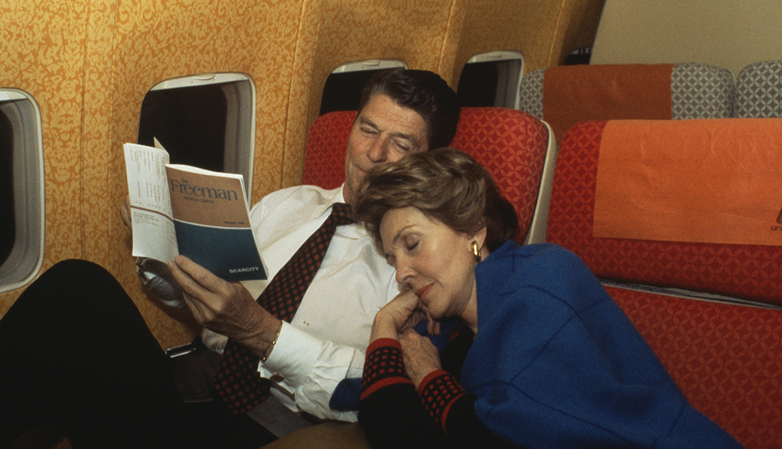 Ronald y Nancy Reagan aborodo de un avión, ella durmiendo y él leyendo un libro