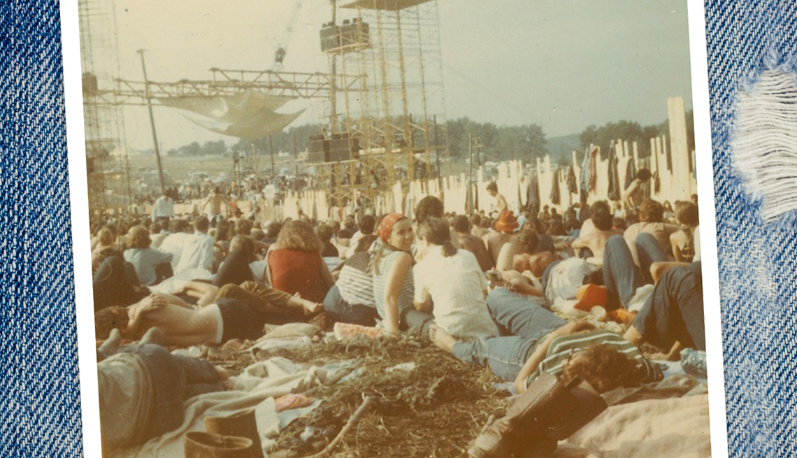 item 2 of Gallery image - small portion of the crowd sitting down at Woodstock mostly with their backs to the camera. in the foreground a girl wearing a red bandana tied over her hair is looking backward at the photographer