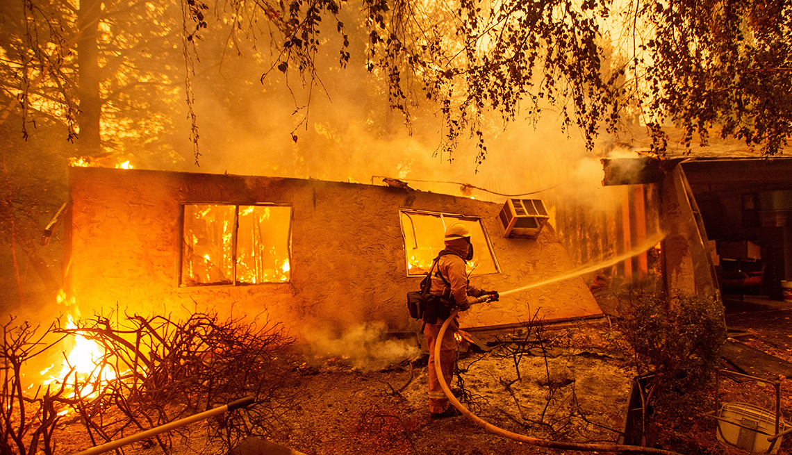 Firefighter fights a wildfire next to what's left of a house