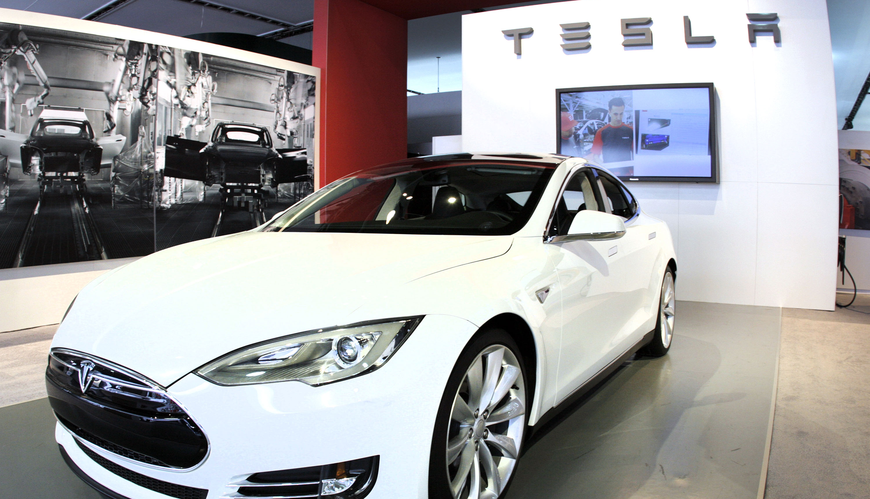 item 2 of Gallery image - a sleek white brand new tesla model s is parked indoors at an auto show in front of a wall showing the tesla brand name