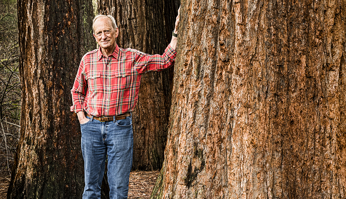 Denis Hayes posa en un bosque con la mano en un gran tronco de árbol