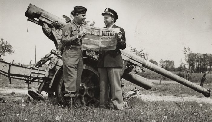 item 2 of Gallery image two united states soldiers reading a newspaper that has the headline victory in front of a large german gun at the end of world war two 