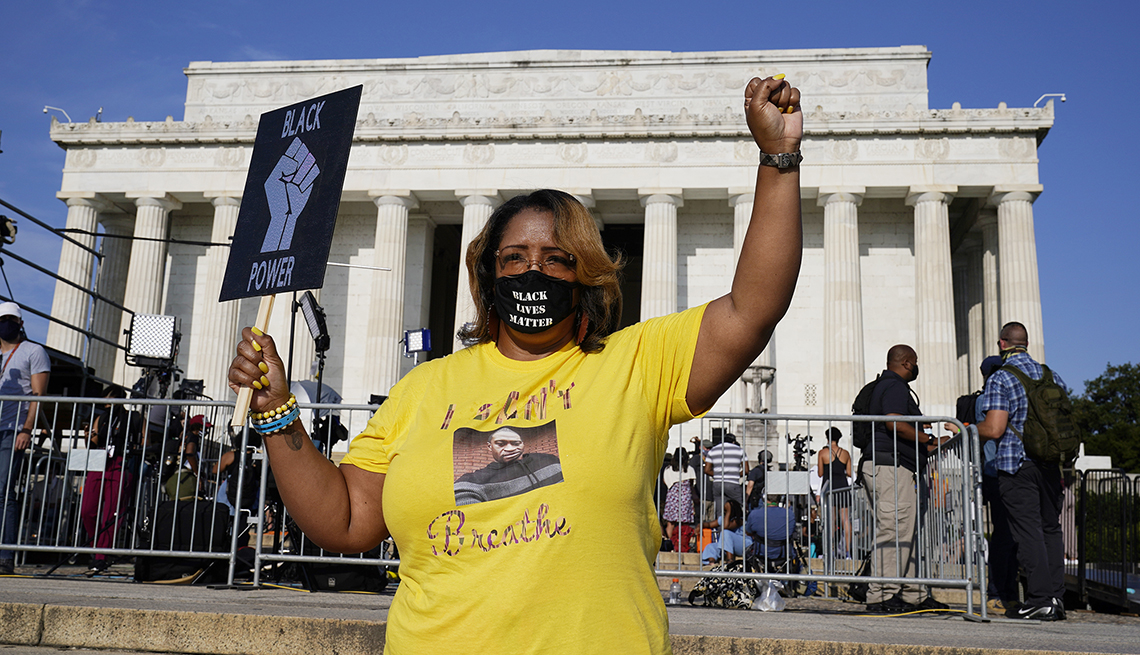 item 4 of Gallery image - A woman in a yellow shirt holds a sign and raises her fist at the march on washington