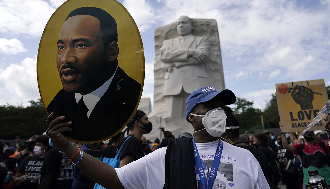 item 12 of Gallery image - A man holds a sign with the face of Martin Luther King Junior on it