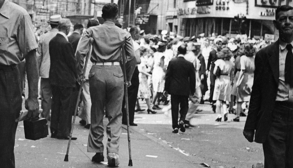 item 7 of Gallery image - Soldado con muletas visto desde atrás en la calle durante la celebración del día V J 