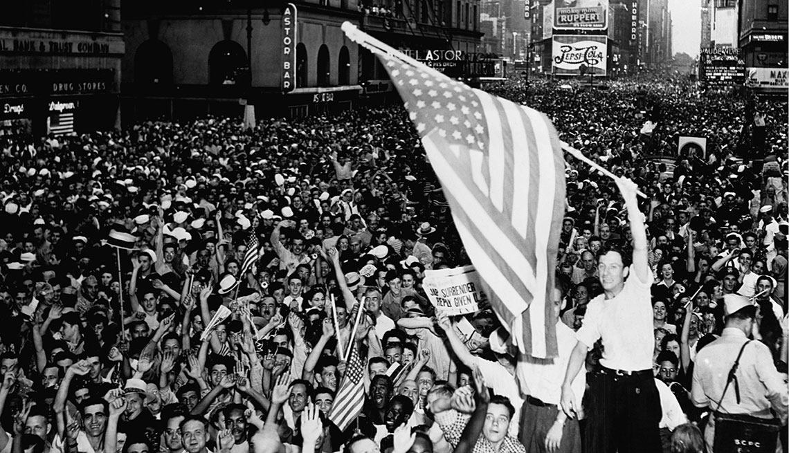 Un hombre ondea una enorme bandera de Estados Unidos en medio de una multitud celebrando la victoria sobre Japón